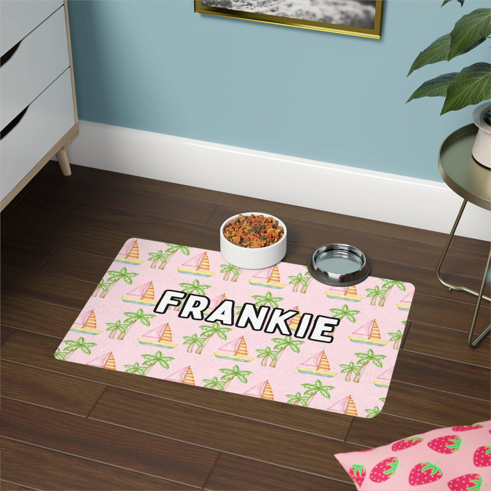 Pet food mat with a pink background featuring an adorable coastal print of pink sailboats and green palm trees, shown on a hardwood floor with a dog bowl and a water bowl, personalized with your pet's name.