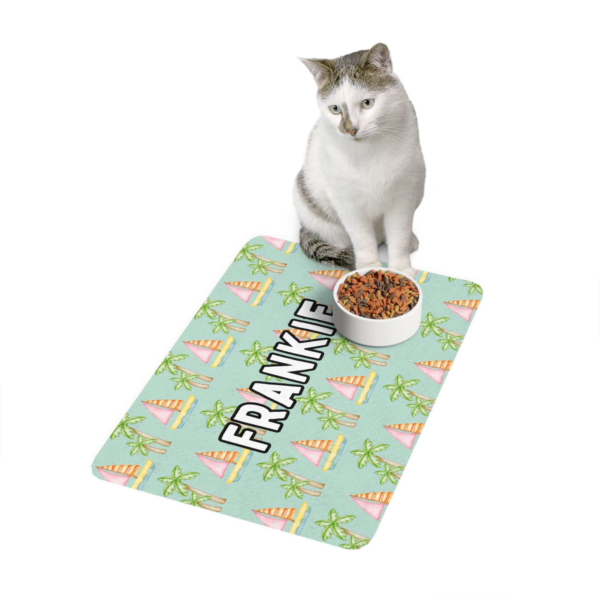 Coastal-themed seafoam pet food mat with sailboats and palm trees, personalized for your pet shown with a cat sitting on the mat and a bowl of cat food.