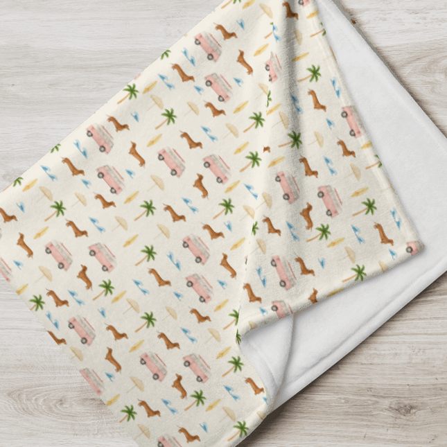 Folded dachshund blanket with beach print featuring wiener dogs, vans, and palm trees